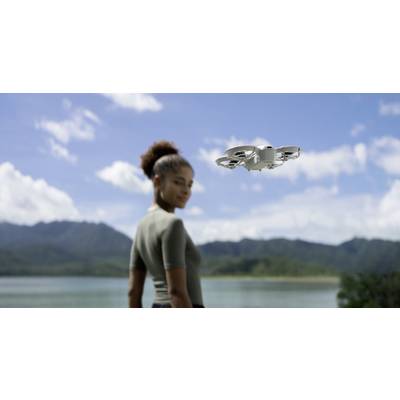 Une femme regarde un drone en vol surplombant un paysage pittoresque de montagnes et de lac.