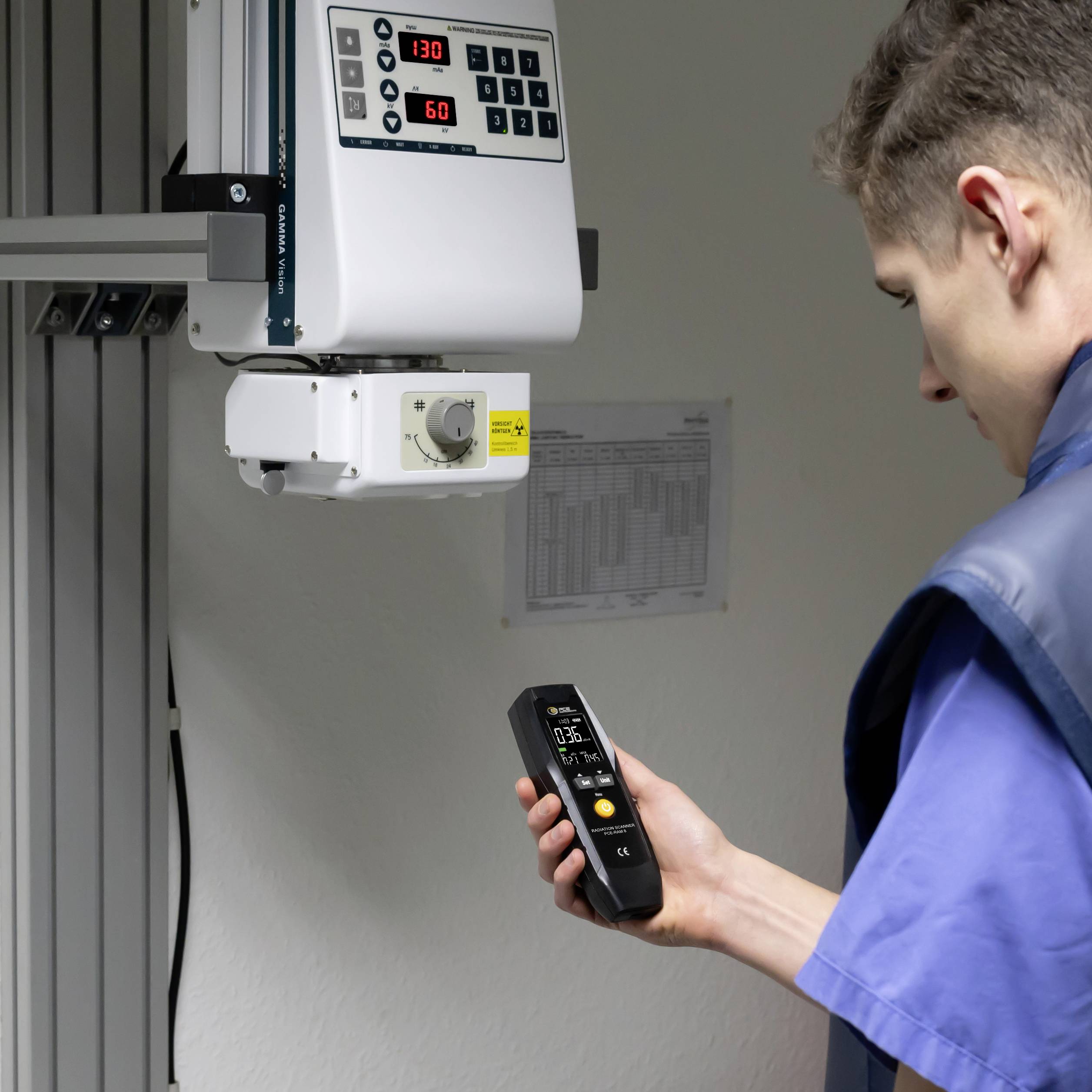 Un technicien en tenue de protection utilise un appareil de mesure portable dans un laboratoire médical, à côté d'un moniteur mural de surveillance.