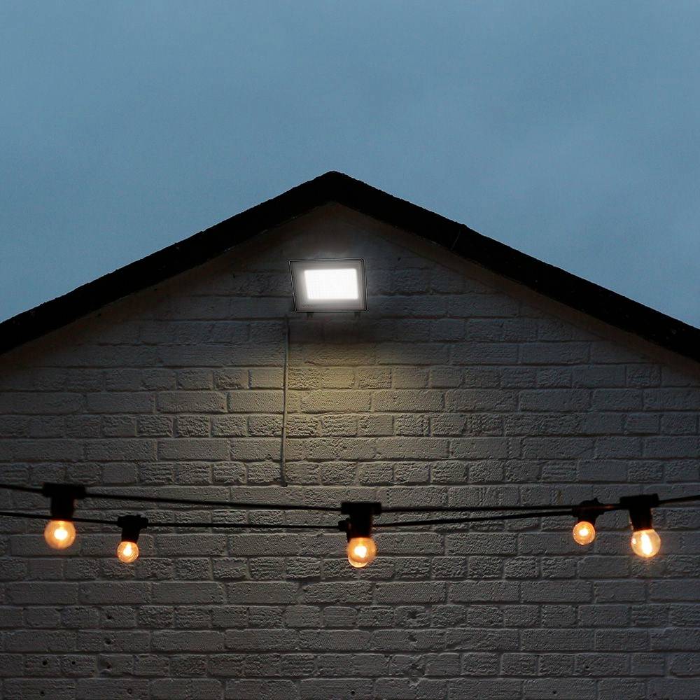 Un bâtiment en briques blanches au crépuscule. Une lampe claire illumine la partie supérieure, avec des ampoules rondes suspendues en rangée en dessous.
