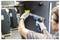 Une personne utilisant un pistolet thermique sur une étiquette jaune fixée à un grand réservoir cylindrique, portant des gants et des lunettes de protection dans un environnement industriel.