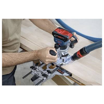 Une personne utilise une défonceuse Bosch sur une surface en bois, avec un tuyau d'aspirateur bleu attaché, la guidant le long du bord pour un façonnage précis.