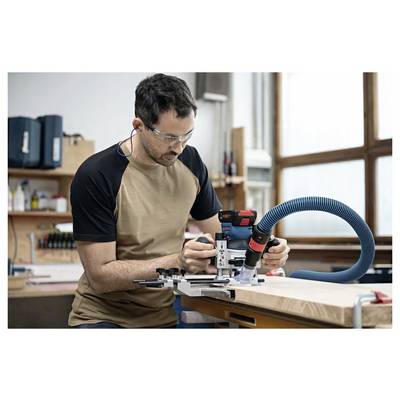 Un homme portant des lunettes de sécurité et des bouchons d'oreilles utilise un outil électrique sur un établi en bois dans un atelier.