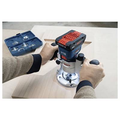 Une personne utilise une défonceuse Bosch pour graver un motif complexe sur une planche en bois, avec des fraises de défonceuse présentées dans un coffret à proximité.