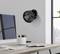 Un ventilateur noir est monté sur le mur d'un bureau moderne. La pièce comprend un bureau avec des accessoires de bureau et une fenêtre offrant une vue sur la ville.