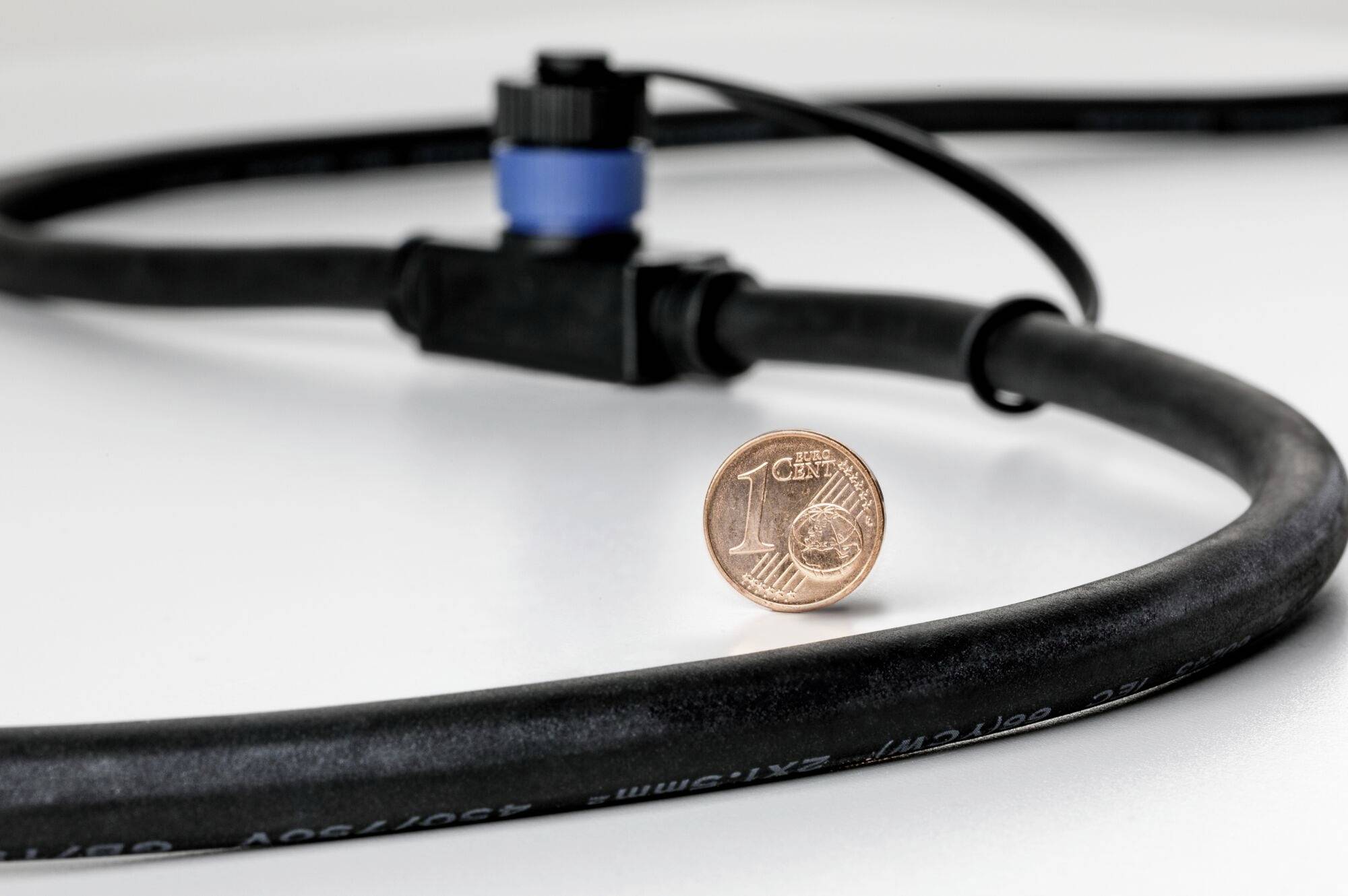 Une pièce de un centime debout sur une table, avec un tuyau noir et un raccord bleu en arrière-plan.