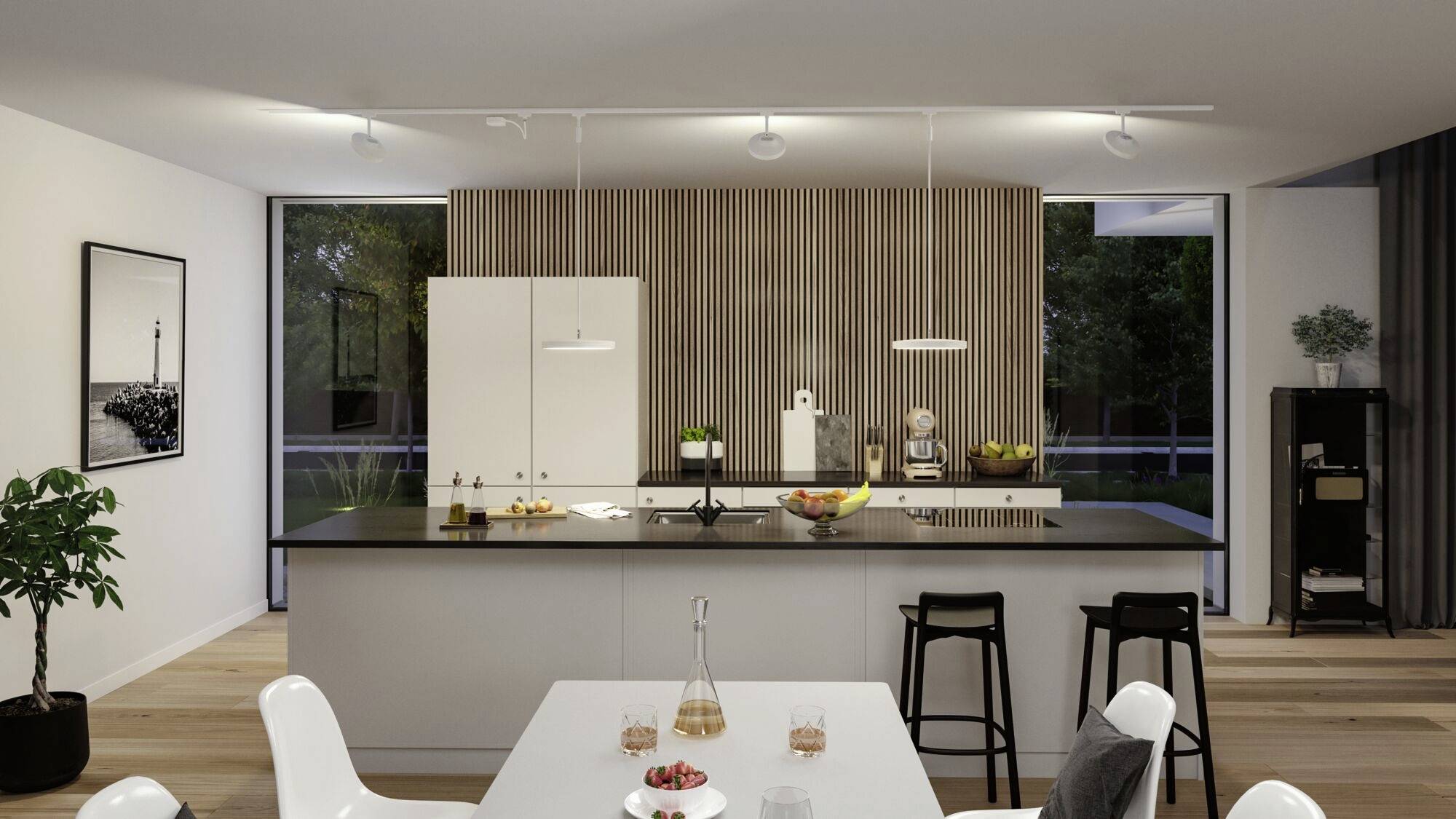 Cuisine moderne avec îlot central, table claire au premier plan, bol de fruits sur le plan de travail, décoration élégante, grandes fenêtres.