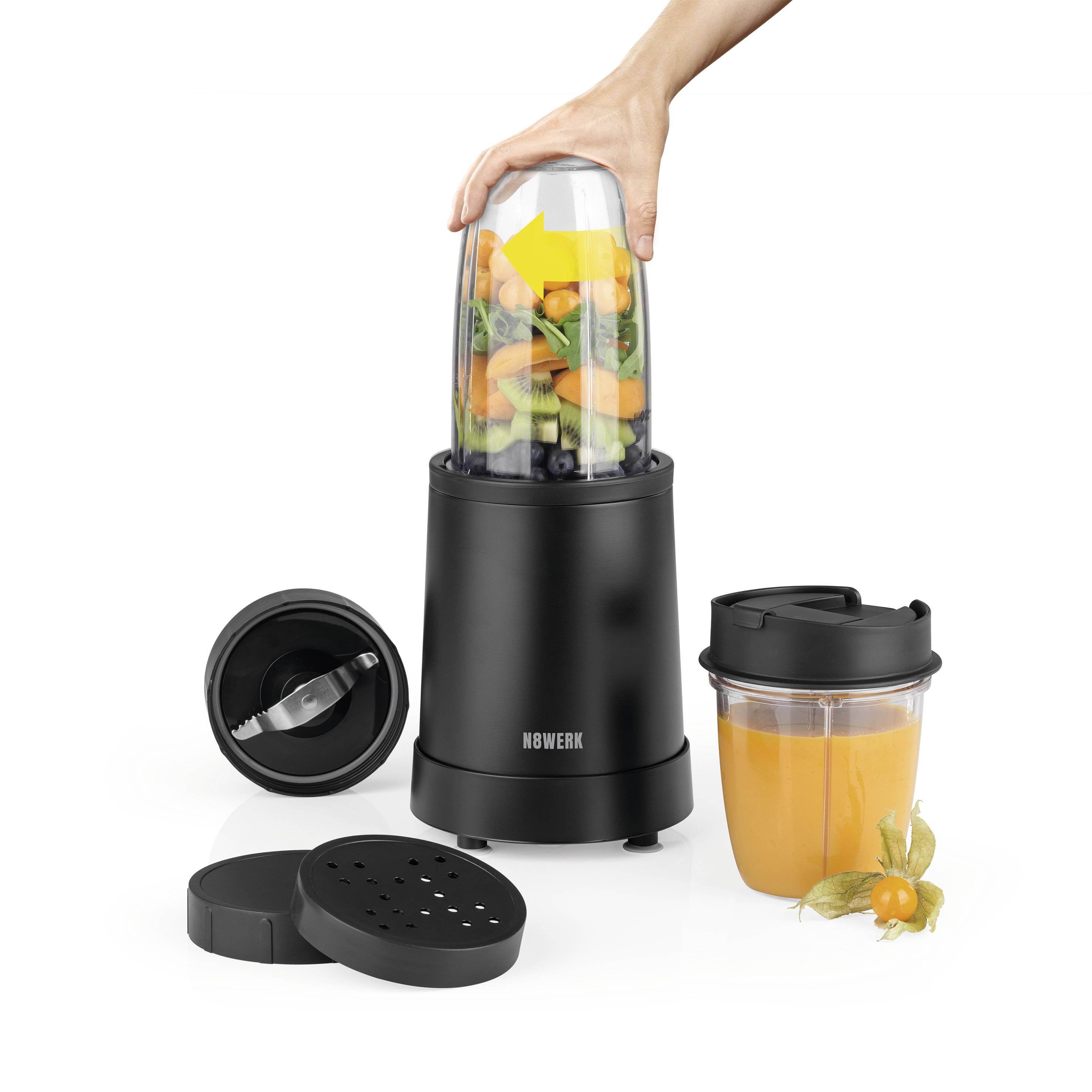 Une main tient le récipient d'un mixeur, rempli de fruits et de légumes, prêt à être mixé. À côté, un autre verre de jus d'orange.