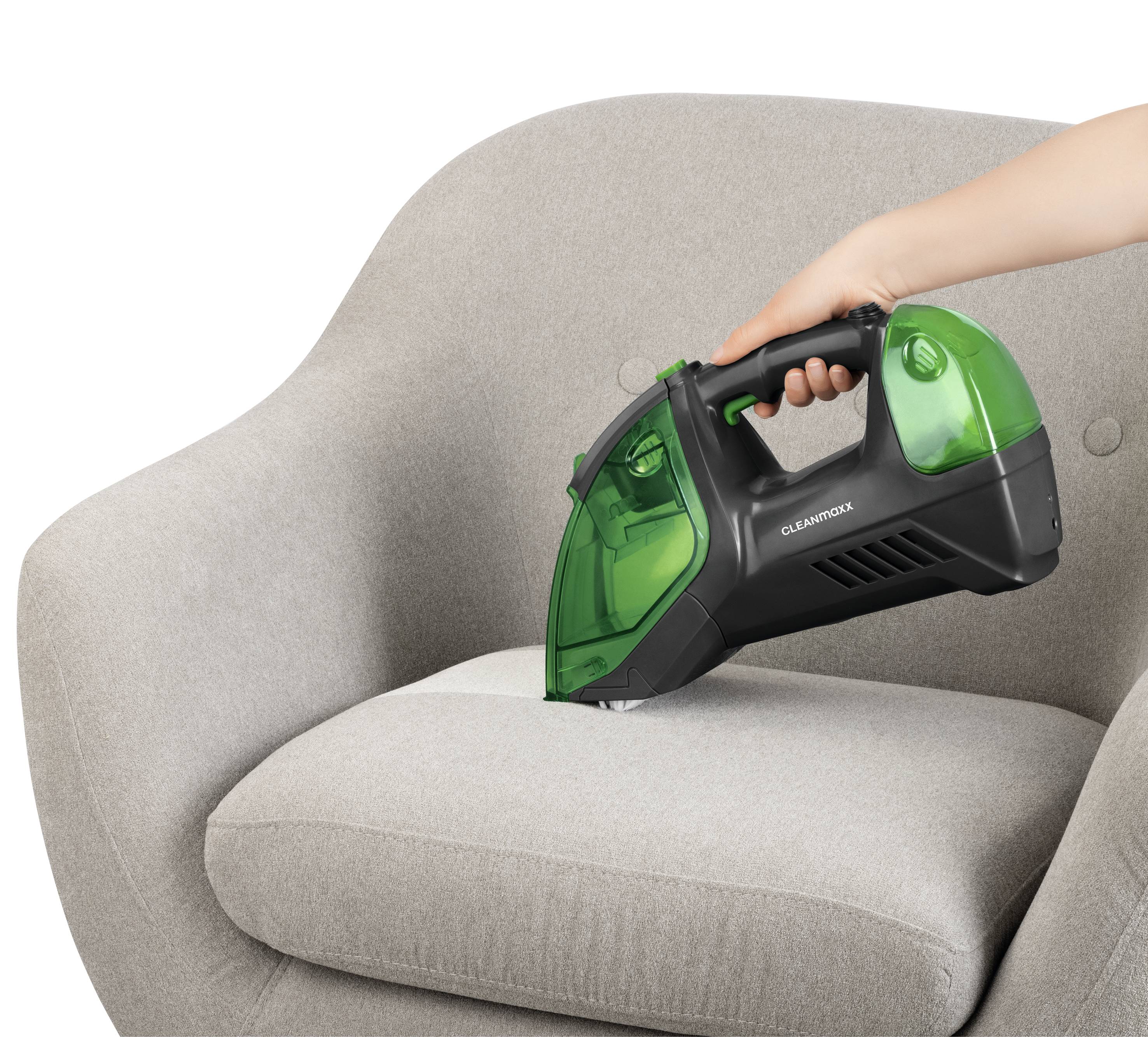 Une personne utilise un aspirateur portable sur un fauteuil gris pour enlever la poussière et les saletés.