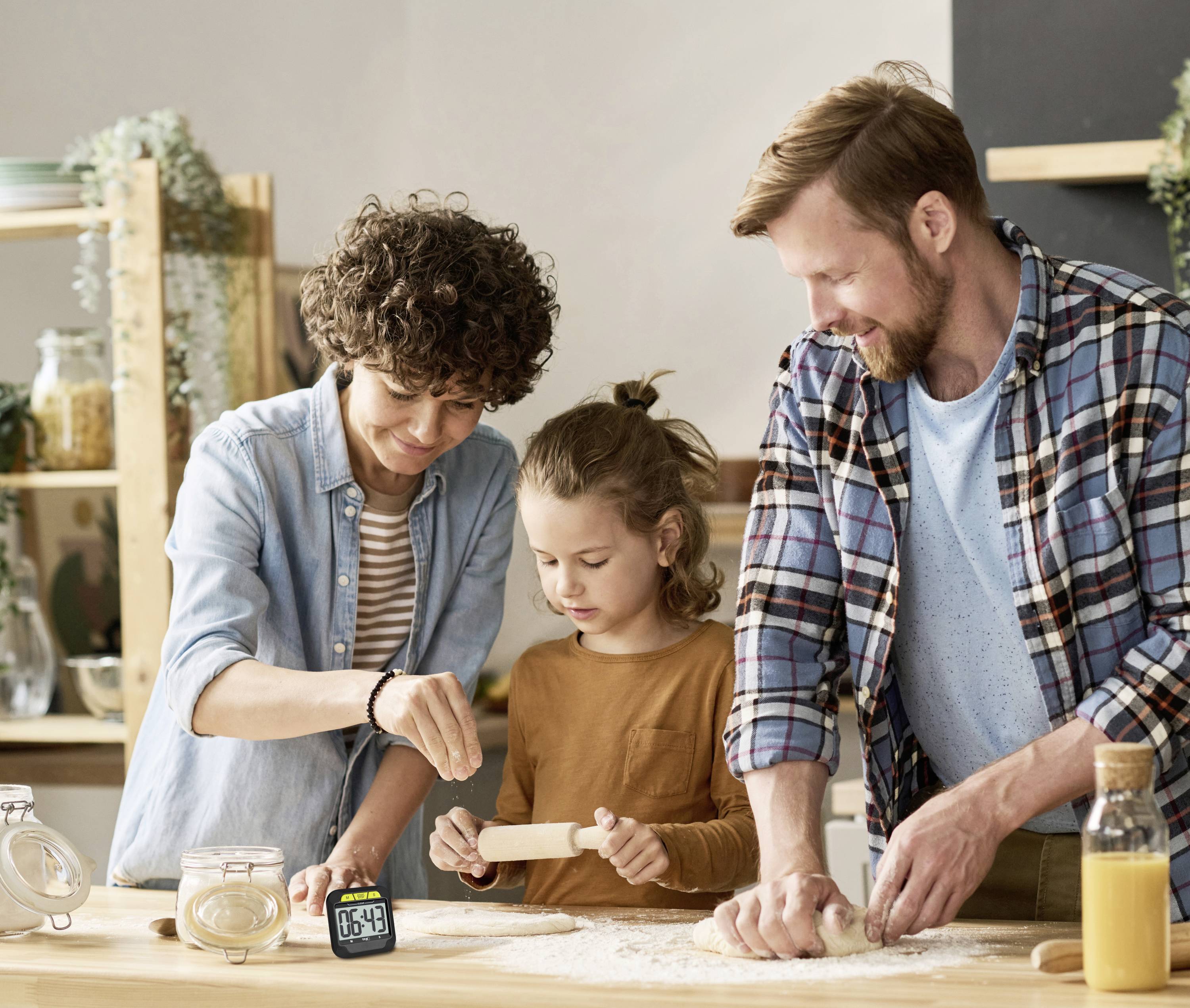 Une famille prépare ensemble des pâtisseries dans la cuisine. Un adulte saupoudre de la farine, un enfant étale la pâte, et un autre adulte l'aide.