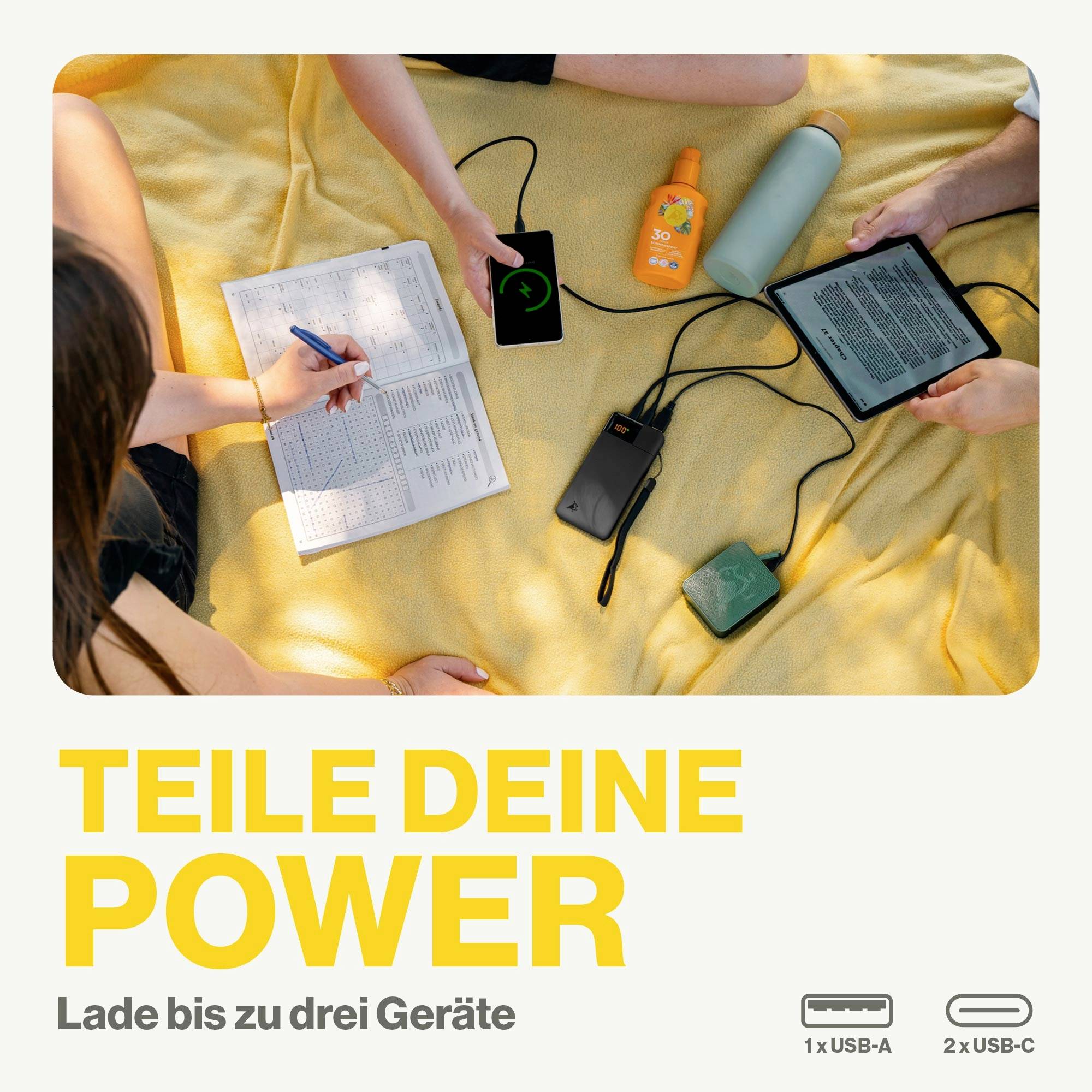 Quatre personnes sont assises sur une couverture, chargent des appareils avec une batterie externe. Texte : 'Partage ta puissance. Charge jusqu'à trois appareils'.
