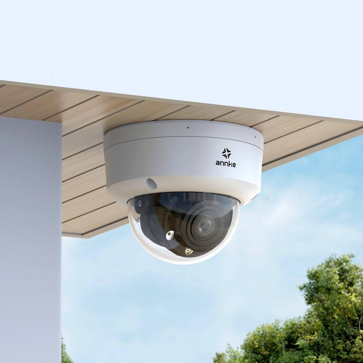 Caméra de surveillance montée sous un toit, orientée vers le bas, avec vue sur un ciel bleu et des arbres verts en arrière-plan.