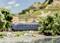 Un train bleu circule par une journée ensoleillée à travers un paysage rural, longeant des arbres verts et des eaux cristallines.