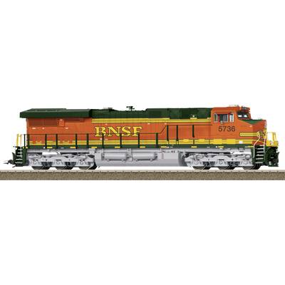 Un train de marchandises orange et vert portant l'inscription 'BNSF' est stationné sur une voie ferrée. La locomotive porte le numéro 5736.