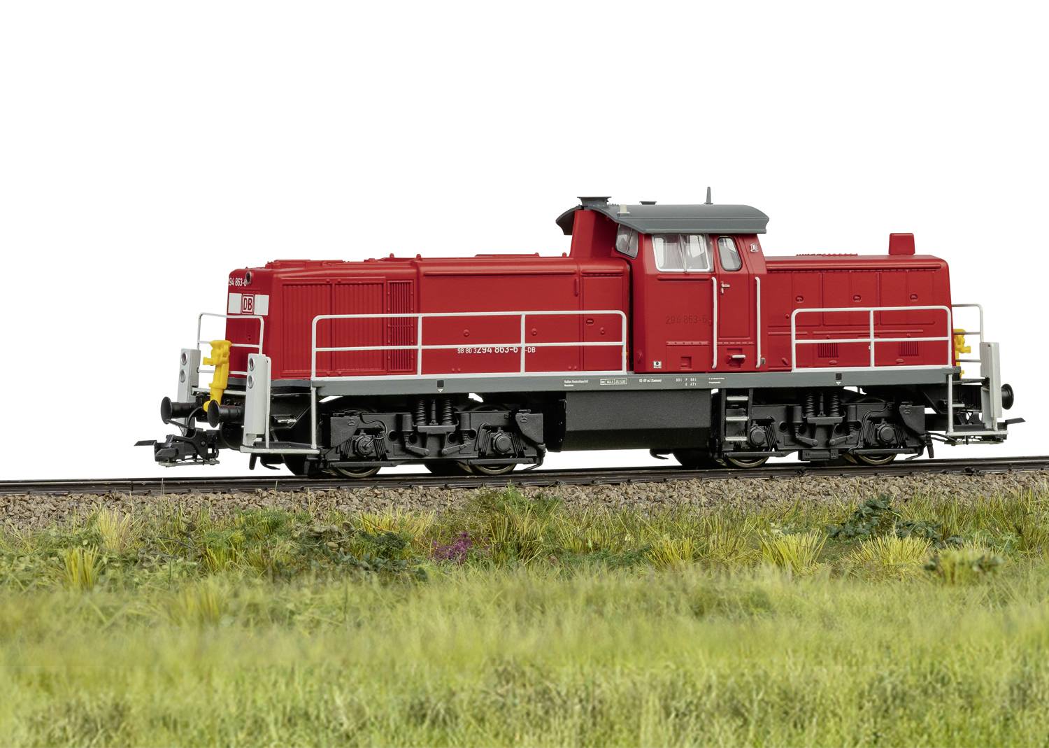 Une locomotive rouge sur une voie ferrée dans un paysage herbeux. La locomotive présente un design simple et moderne.