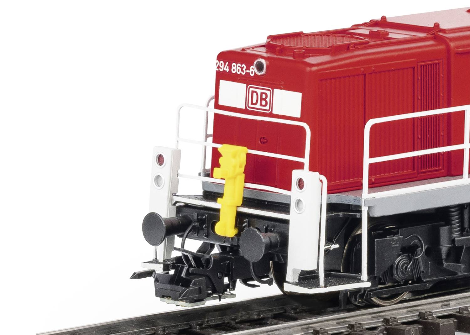 Un modèle rouge de locomotive diesel de la DB sur un réseau ferroviaire miniature, détaillé avec des garde-corps blancs et un tuyau de frein jaune.