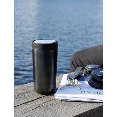 Un gobelet isotherme noir sur une table en bois près de l'eau, à côté d'un trousseau de clés et d'écouteurs posés sur un magazine.