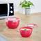 Bols en plastique rouge avec couvercles sur un plan de travail de cuisine. Un bol est ouvert. Une plante et un four micro-ondes sont visibles en arrière-plan.