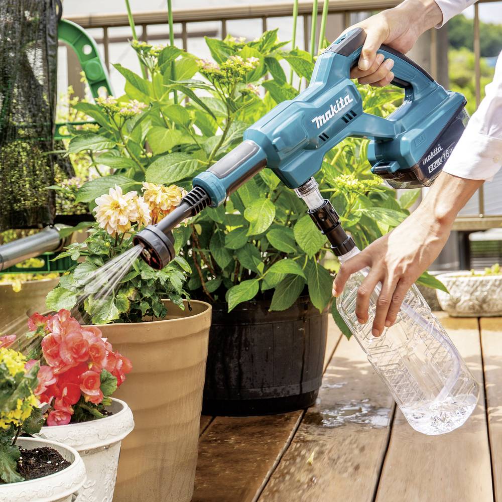 Une personne tient un nettoyeur haute pression portable bleu et arrose des plantes sur une terrasse en bois avec un réservoir d'eau supplémentaire.