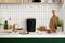 Machine à pain noire sur un plan de travail de cuisine, entourée de pain frais, de charcuterie et de plantes. Des planches en bois et de la vaisselle décorent l'espace.