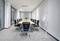 Salle de conférence moderne avec une longue table en bois, entourée de chaises de bureau noires. Un ventilateur blanc sur pied est installé contre le mur.