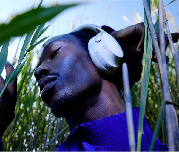 Personne aux yeux fermés portant des écouteurs, entourée de hautes herbes, dans une pose détendue.