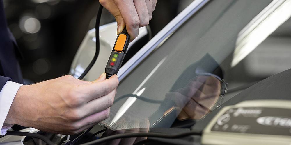Un mécanicien utilise un appareil pour vérifier le pare-brise d'une voiture. L'appareil affiche un indicateur LED avec plusieurs couleurs.
