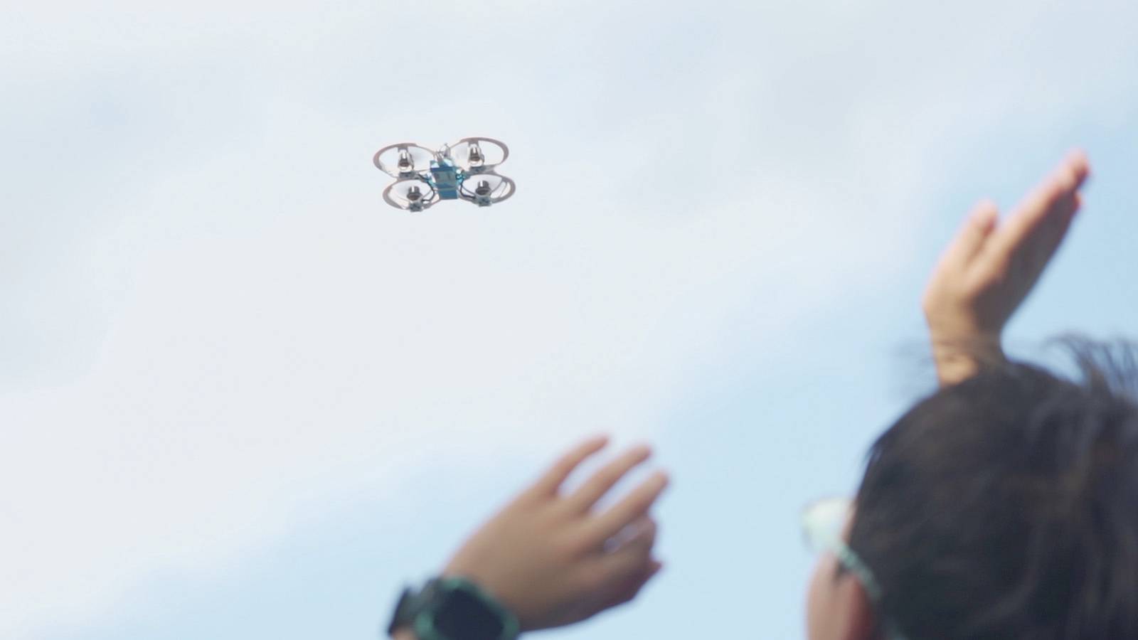 Un enfant regarde le ciel et fait signe à un petit drone en vol.