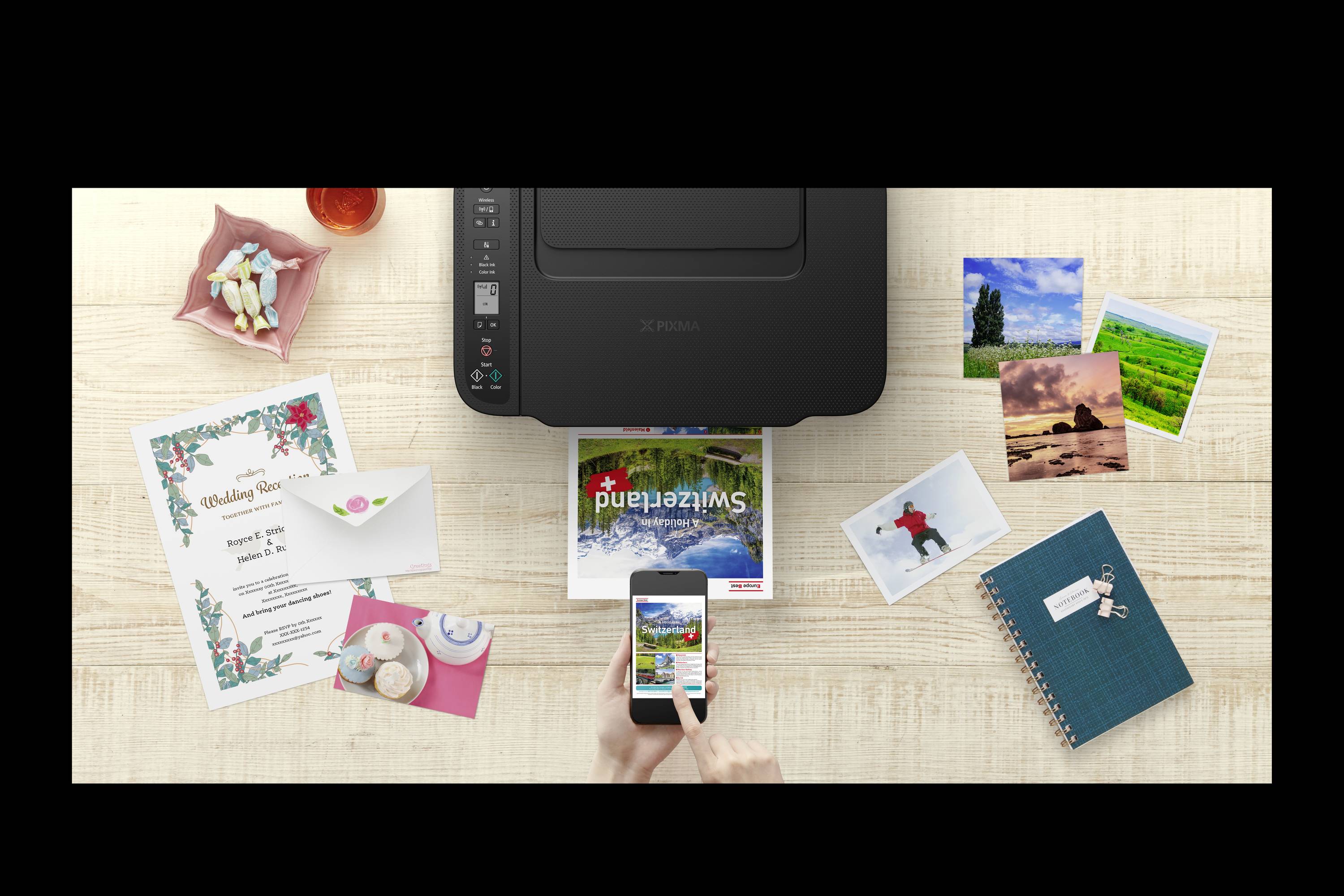 Imprimante sur une table, entourée de photos, d'une invitation de mariage, d'un carnet de notes et d'un smartphone qui imprime une photo.