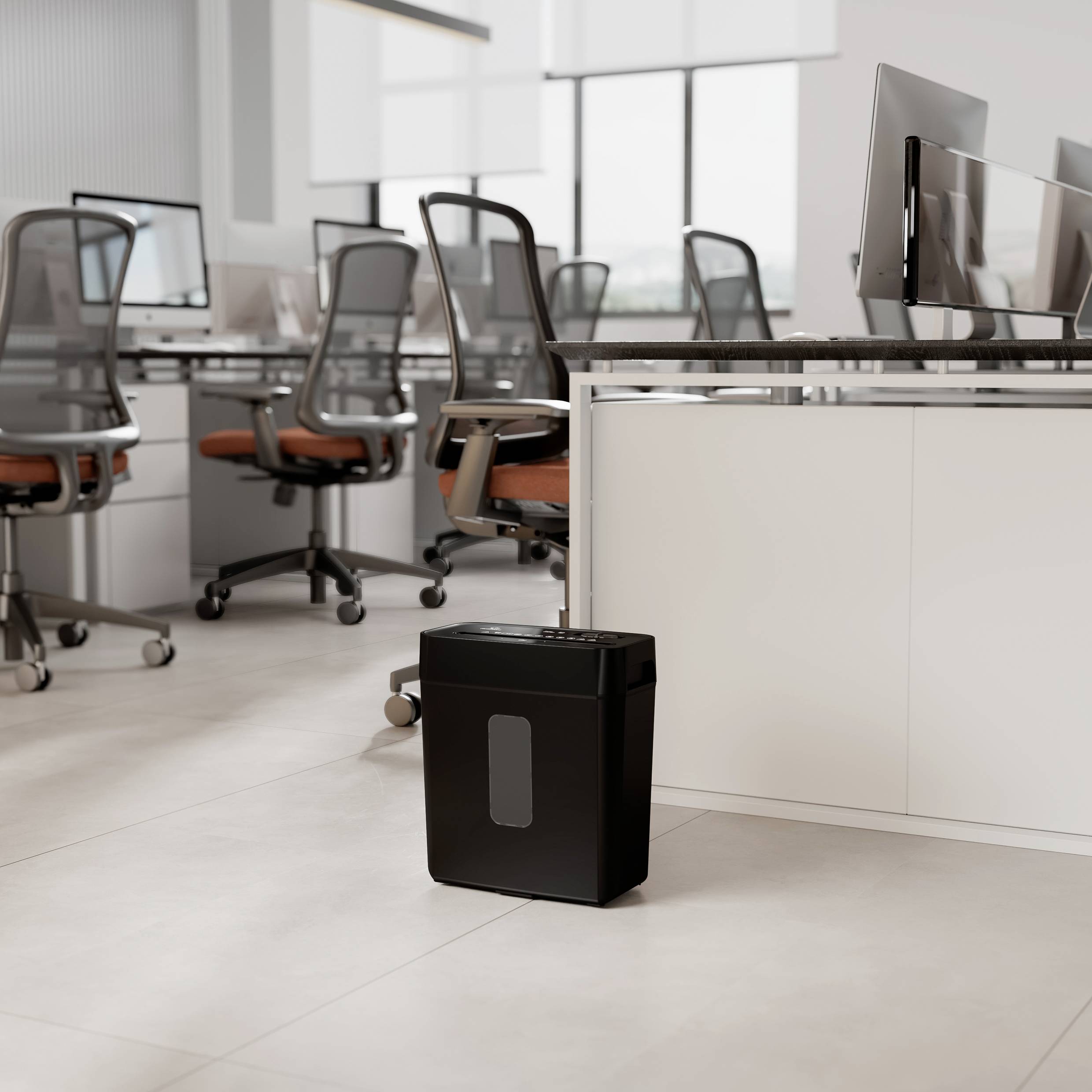 Un bureau avec plusieurs bureaux et ordinateurs ; au premier plan, un destructeur de documents noir est posé au sol.