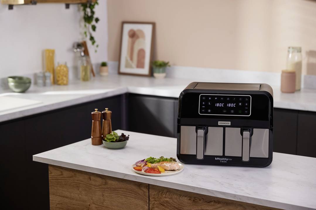 Une cuisine moderne avec une friteuse à air chaud sur le plan de travail. Devant se trouve une assiette avec du saumon et des légumes.
