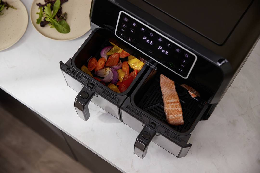 Une friteuse à air chaud à deux compartiments : un pour le saumon, l'autre pour les légumes. Panneau de commande lumineux en haut de l'appareil.