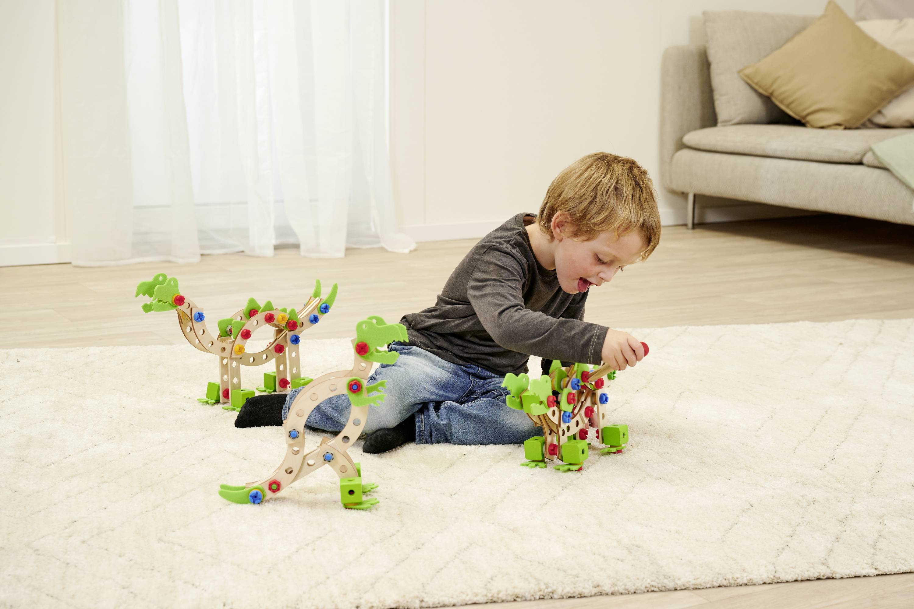 Un enfant joue sur un tapis du salon avec des blocs de construction en bois colorés, assemblés pour former des formes de dinosaures.