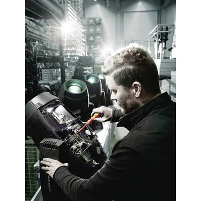 Un homme répare un boîtier de phare avec un tournevis dans un hall d'usine. D'autres phares sont visibles en arrière-plan.
