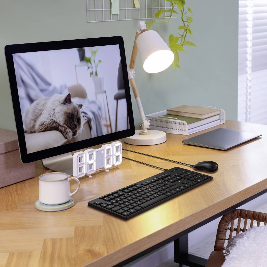 Un bureau avec un écran d'ordinateur affichant un chat, une horloge numérique, une tasse, une lampe et un clavier.