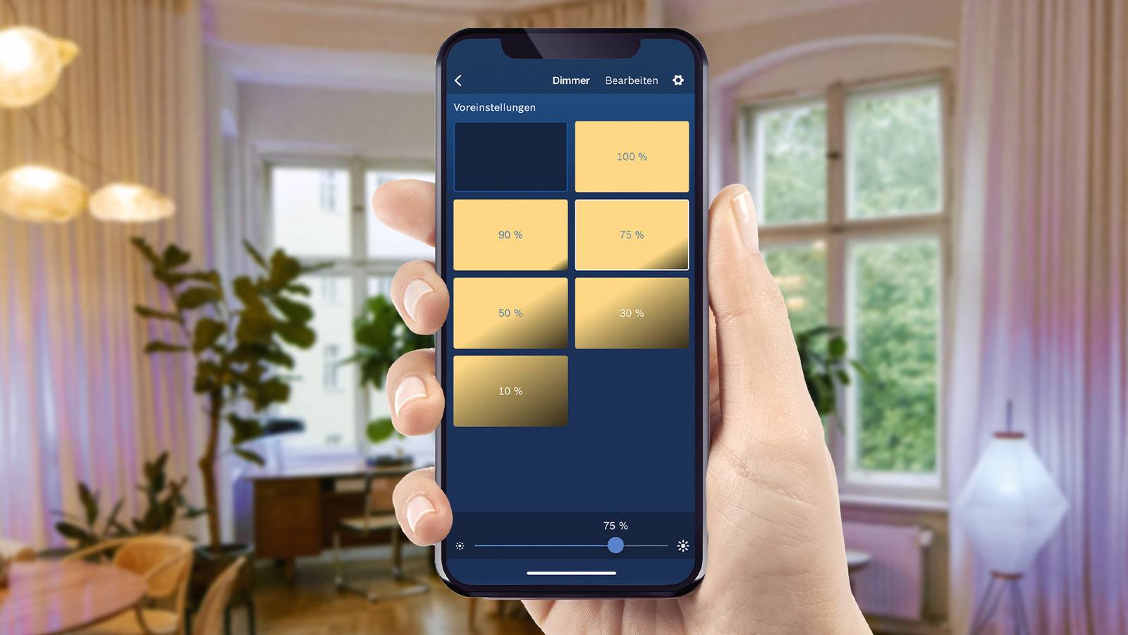 Un smartphone est tenu dans un salon et affiche une application permettant de contrôler l'intensité lumineuse en pourcentage.