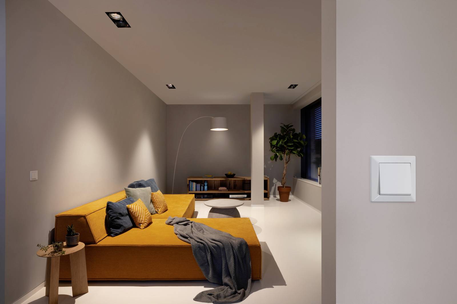 Un salon moderne avec un canapé orange, des coussins bleus, un lampadaire et une plante. Un interrupteur est visible sur le mur.