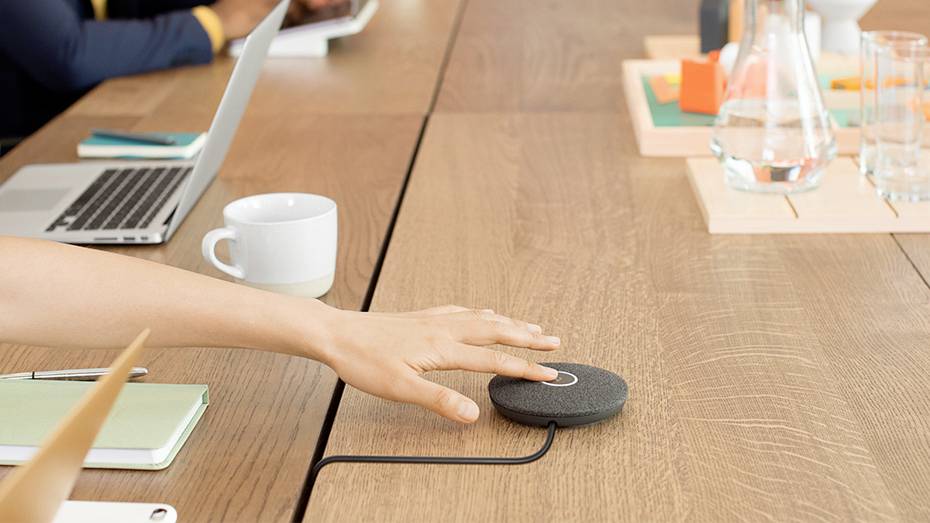 Une personne active un microphone de conférence sur une table avec un ordinateur portable et un cahier, prête pour une réunion.