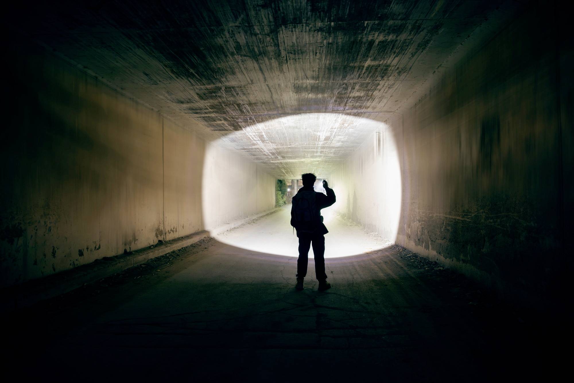 Une personne se tient dans un tunnel éclairé et regarde vers l'extérieur. Silhouette devant une sortie lumineuse.