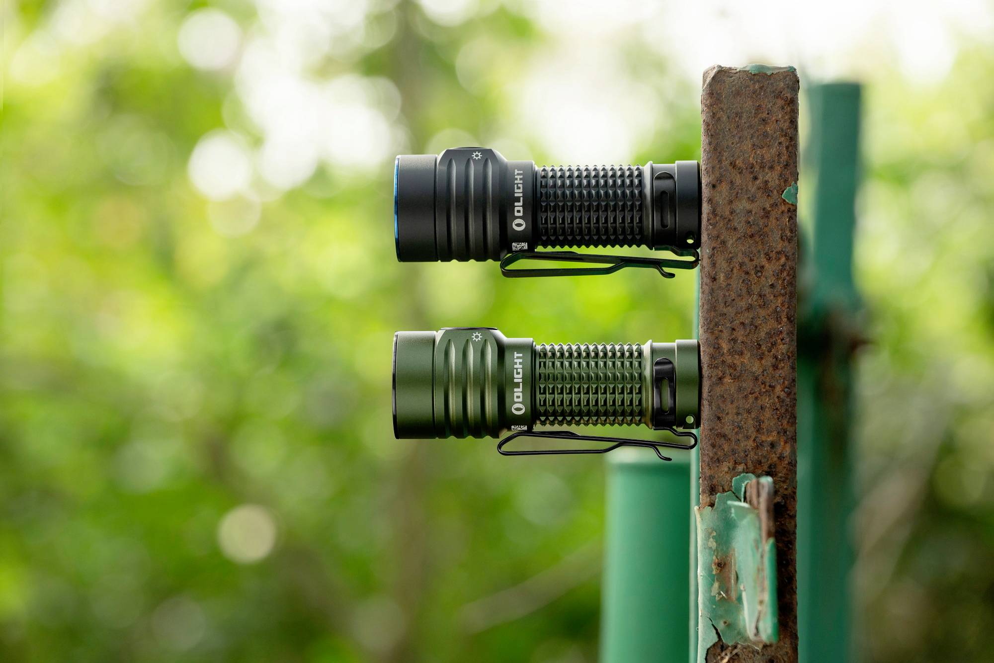 Deux lampes de poche sont fixées à un poteau métallique rouillé, devant un arrière-plan d'arbres verts flous.