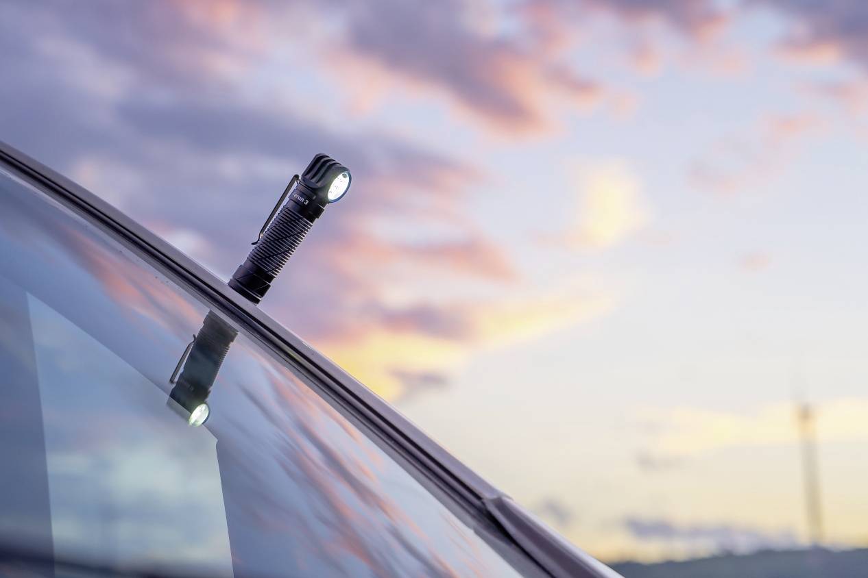 Lampe de poche sur le toit d'une voiture au coucher du soleil, avec un ciel aux couleurs pastel en arrière-plan, créant une ambiance douce du soir.