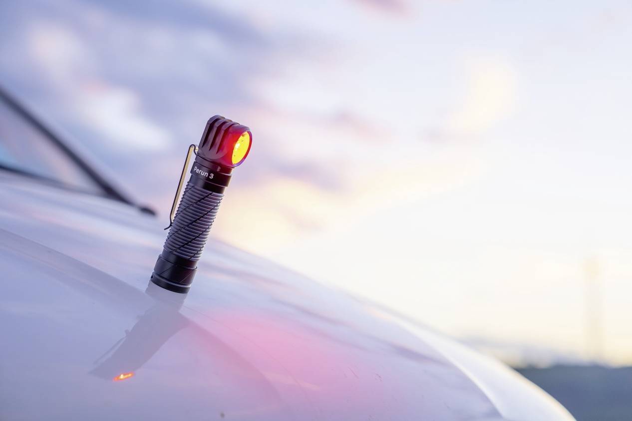 Une petite lampe de poche à lumière rouge est posée sur une surface lisse et brillante au coucher du soleil.