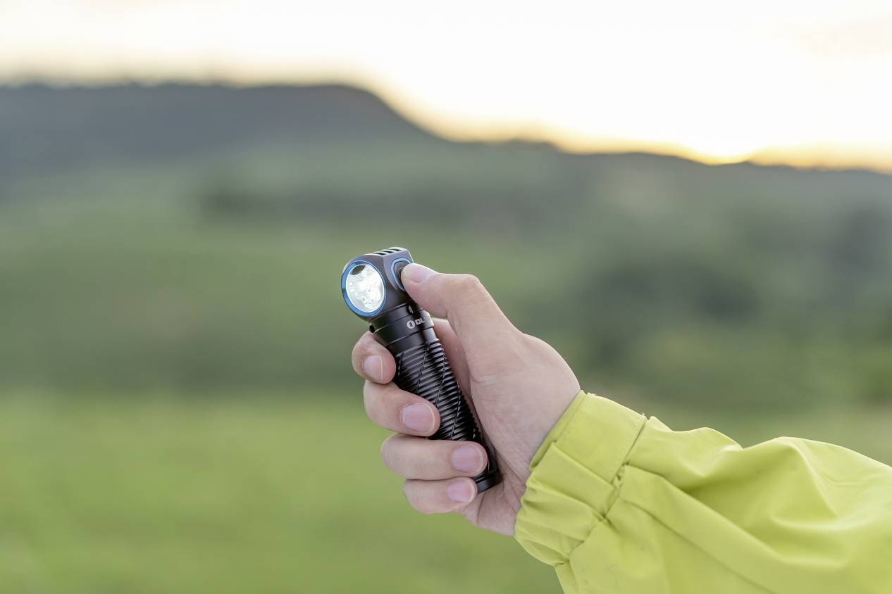 Une personne tient une lampe de poche à la main. La lampe de poche éclaire dans un environnement naturel au crépuscule.