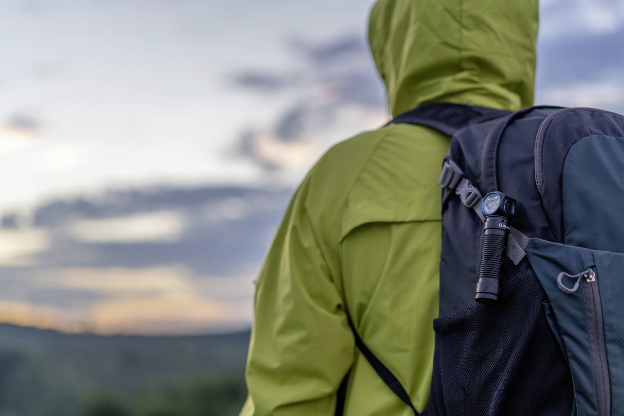 Une personne portant un imperméable jaune et un sac à dos regarde au loin ; en arrière-plan, on aperçoit un crépuscule nuageux.