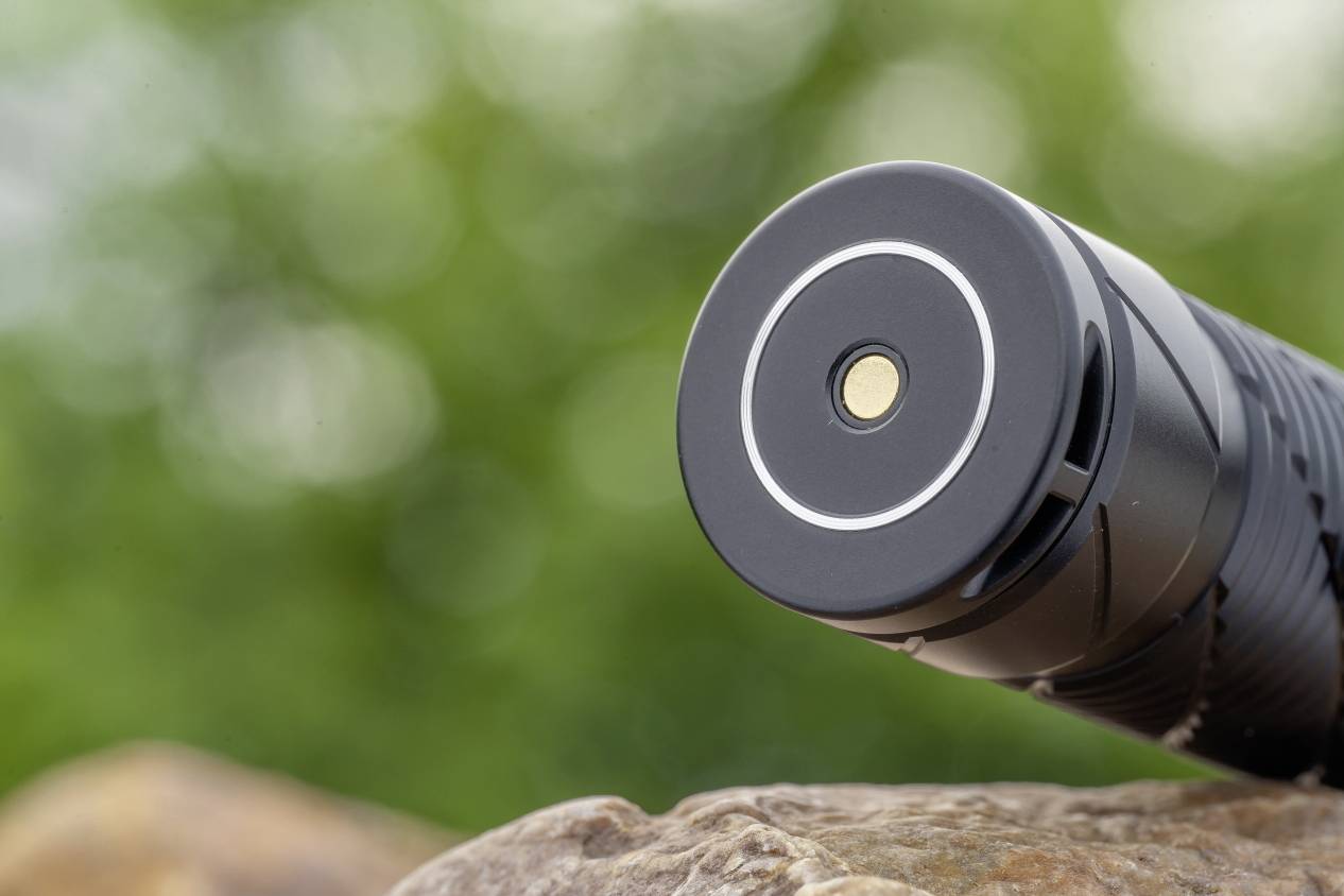 Une lampe de poche est posée sur un rocher avec un arrière-plan vert et flou. La mise au point est sur l'extrémité avant de la lampe de poche.