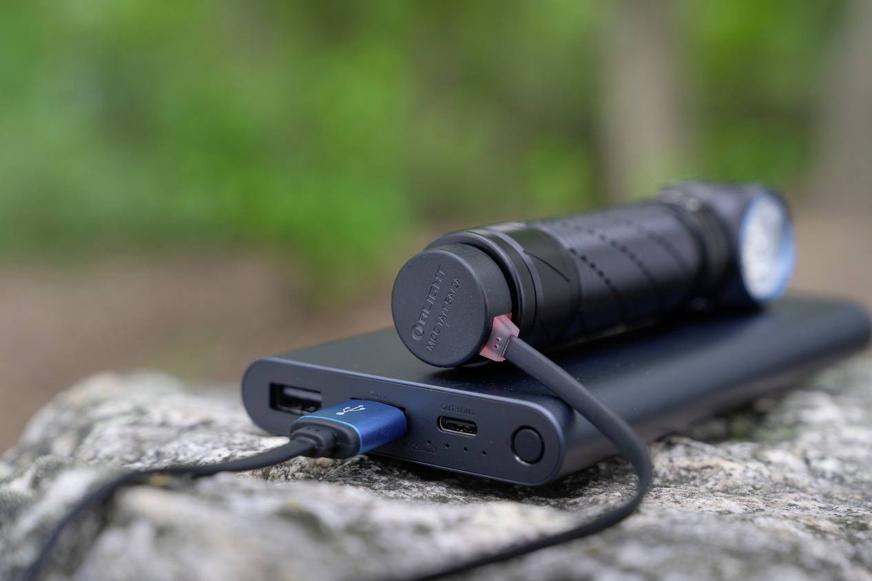 Une batterie externe posée sur une pierre avec une lampe de poche connectée, entourée d'un arrière-plan vert flou.