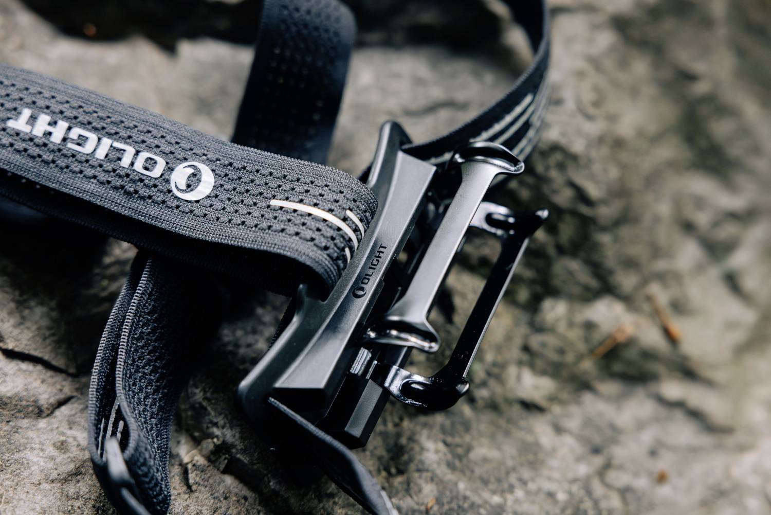 Une boucle de ceinture noire portant l'inscription 'Olight' est posée sur une pierre grise et rugueuse.