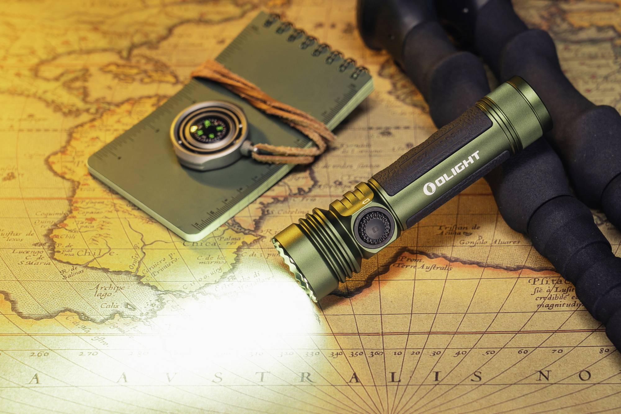 Une lampe de poche illumine une carte du monde antique. À côté de la lampe se trouvent un carnet de notes et une boussole. Thème de l'exploration.