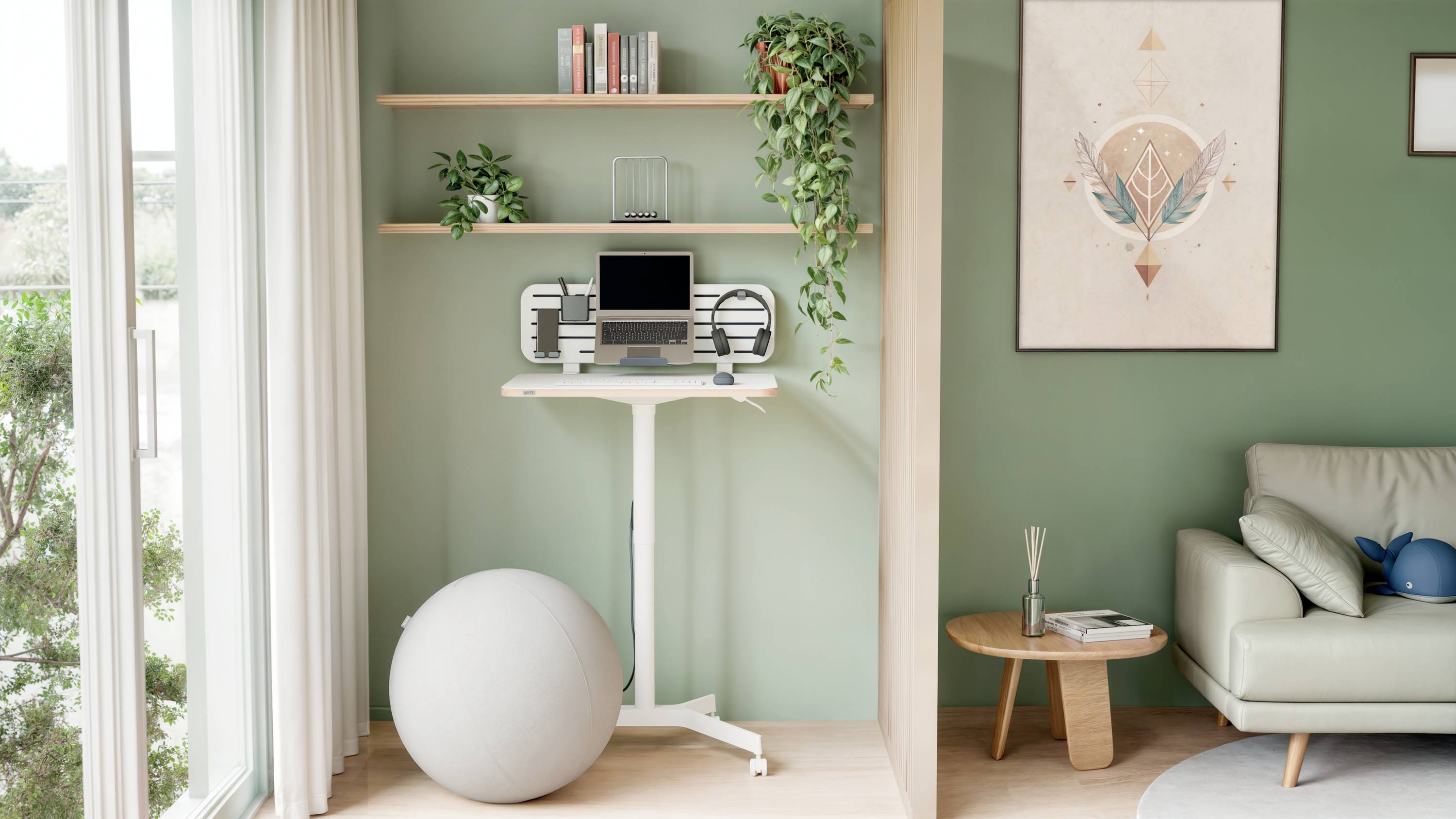 Bureau debout avec un ordinateur portable et un écran dans une pièce minimaliste aux murs verts, avec des plantes et un ballon de gym, à côté d'une fenêtre laissant entrer la lumière du jour.