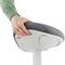 Une personne tient l'assise d'une chaise moderne et ergonomique recouverte de tissu gris, montée sur un socle blanc.