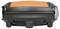 Un petit grill électrique portable avec un couvercle orange et un boîtier noir, idéal pour griller en déplacement.
